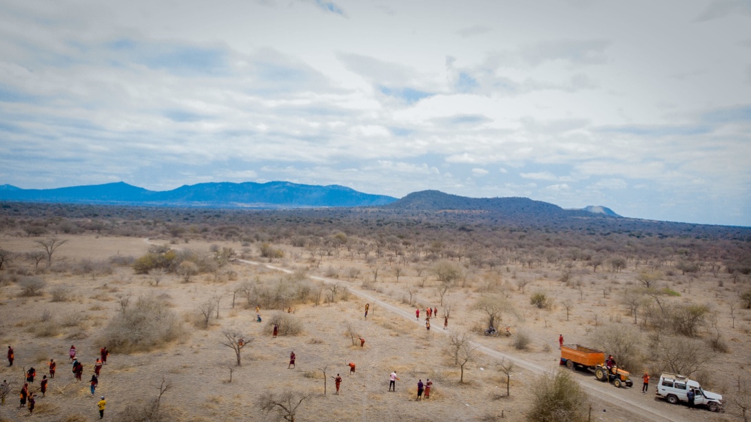 Aerial view of a group of people in an arid field, next to a road.